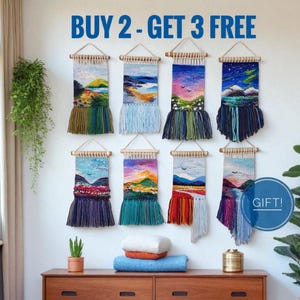 May include: Eight woven wall hangings with landscape designs, each with a unique colour palette and fringe. The text "BUY 2 - GET 3 FREE" is displayed at the top. A small plant and decorative items sit on a wooden dresser.
