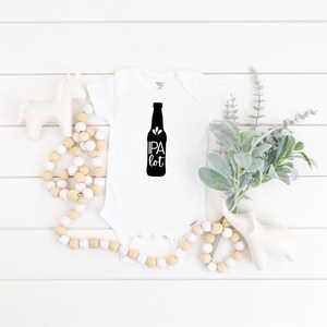 Op de afbeelding: Witte baby romper met een zwarte afbeelding van een bierfles met de tekst "IPA lot" erop.