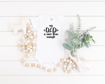 May include: White baby onesie with black text that reads "my dad is more than enough."