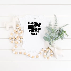 Könnte beinhalten: Weißer Baby-Strampler mit schwarzem Text, der "DIABOLICAL, DEMENTED, SUBHUMAN, POO POO HEAD" lautet.