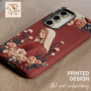 May include: A phone case with a printed design featuring an embroidered-style illustration of a woman with a white head covering, surrounded by flowers. The case is primarily burgundy with floral accents and the text "PRINTED DESIGN Not real embroidery".