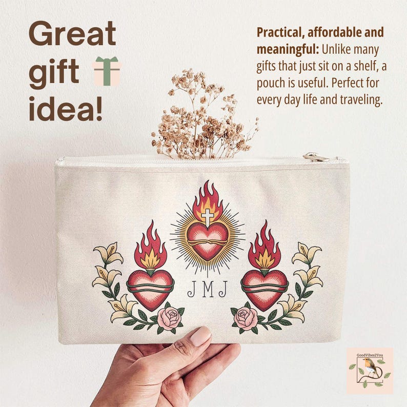 May include: A beige canvas pouch with a zipper closure. The pouch features a central heart design with a cross, surrounded by flames and floral elements. Text on the pouch reads "Great gift idea!" and "JMJ".
