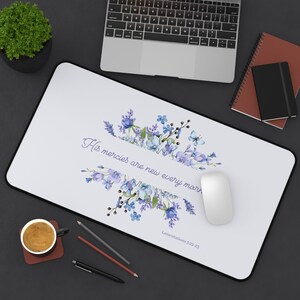 May include: White desk mat with a floral design in shades of blue and purple. The text "His mercies are new every morning" is written in a cursive font. The Bible verse "Lamentations 3:22-23" is printed below the floral design.