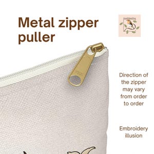 May include: Close-up of a beige pouch with a gold metal zipper puller. The text "Metal zipper puller" is visible. Additional text indicates the zipper direction may vary and mentions an embroidery illusion.