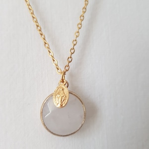 May include: A gold chain necklace with a pale pink oval pendant and a small gold charm. The charm features a religious figure.