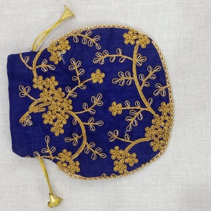 May include: A navy blue drawstring pouch with gold floral embroidery. The pouch has a rounded shape with a gold beaded trim and gold drawstring cords. The floral design is centered on the pouch and is made up of flowers and leaves.