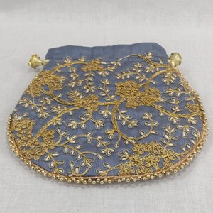 Könnte beinhalten: Ein grauer Beutel mit Kordelzug, goldener Blumenstickerei und Perlenbesatz. Der Beutel hat einen abgerundeten Boden und goldene Akzente am Kordelzugverschluss. Die Stickerei zeigt ein zartes Blumenmuster.