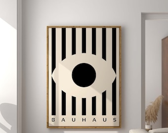 May include: Black and white abstract art print featuring a large eye shape and the word "BAUHHAUS" in black text. The print is framed and hanging on a white wall in a modern living room.