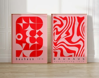 May include: Two framed posters with a pink background and red geometric designs. The poster on the left has a geometric pattern of circles, squares, and triangles. The poster on the right has a swirling, abstract pattern. Both posters have the text "bauhaus 1919" at the bottom.