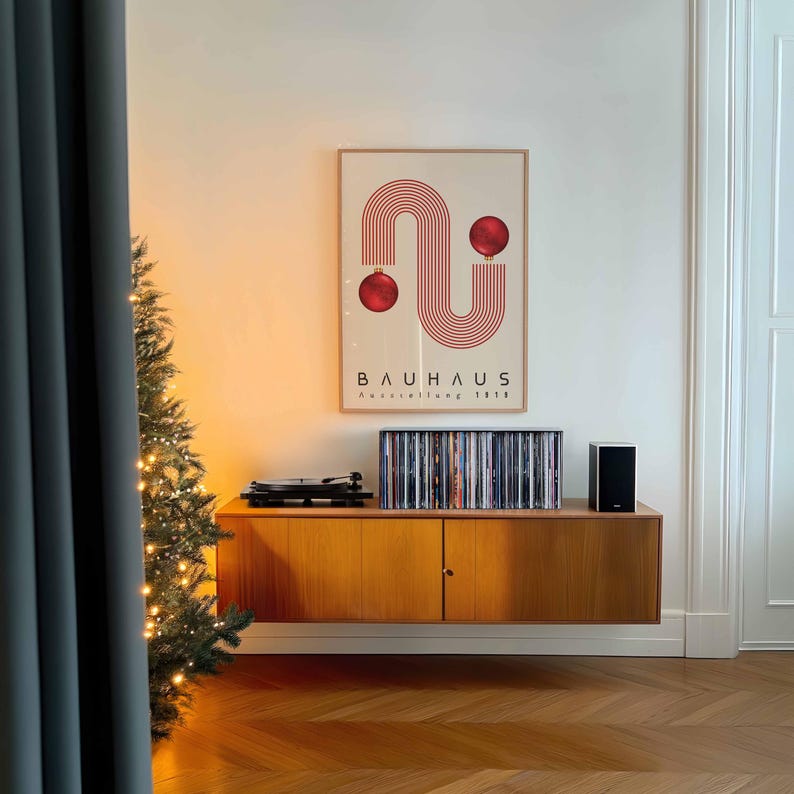 May include: A framed poster featuring a red line graphic forming an S-shape with two red spheres, labeled BAUHAUS Ausstellung 1923. The poster hangs above a wooden cabinet holding a record player, a row of vinyl records, and a black speaker.