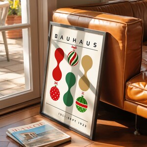 May include: A framed Bauhaus poster with a cream background featuring the text BAUHAUS at the top and JULI-SEPT 1923 at the bottom. The design includes three vertical columns of abstract shapes and Christmas ornaments in red, green, and gold.