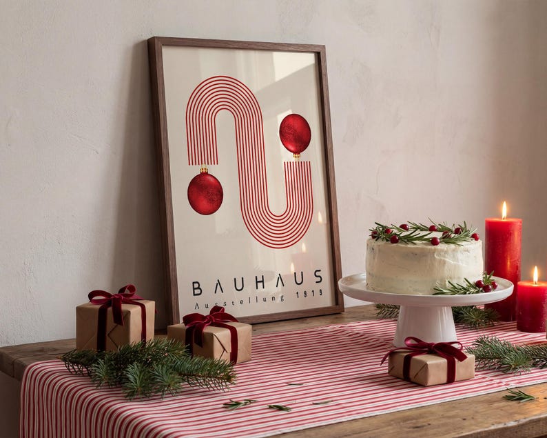 May include: A framed poster featuring red concentric lines forming an S-shape with two red ornaments, labeled BAUHAUS Ausstellung 1919. The print is displayed on a table with a striped runner, a frosted cake, and small gift boxes tied with red velvet ribbons.