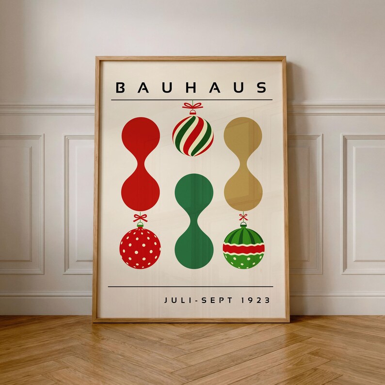May include: A rectangular poster in a light wood frame featuring the text BAUHAUS at the top and JULI-SEPT 1923 at the bottom. The design displays six abstract shapes resembling Christmas ornaments in red, green, and gold, arranged in three vertical columns against a cream background.