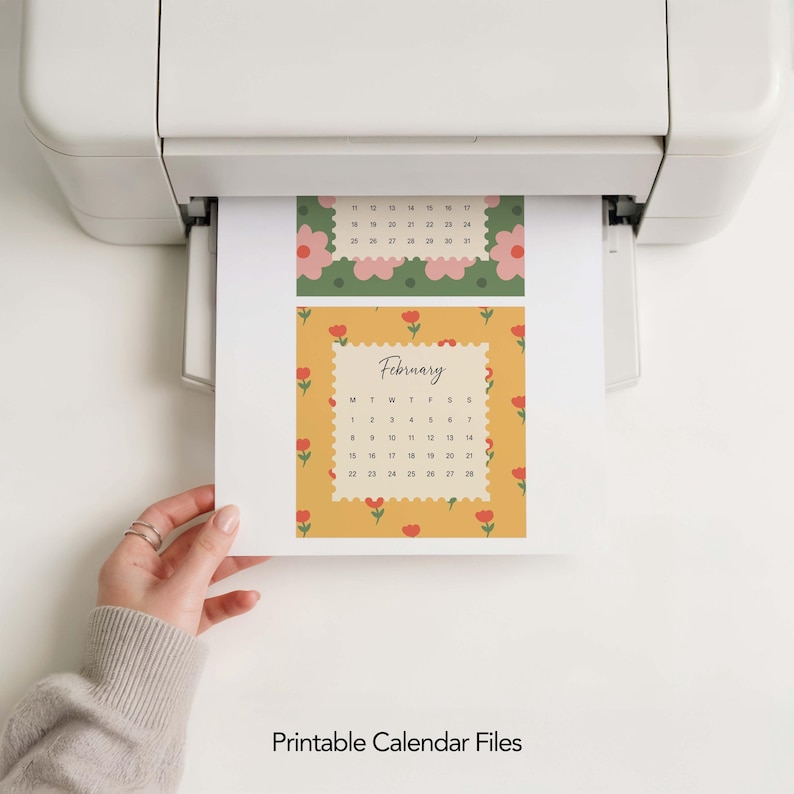 May include: A white printer outputting a sheet of paper featuring two calendar designs. The top section has a green background with pink flowers, while the bottom section displays a yellow background with red tulips and the text February.