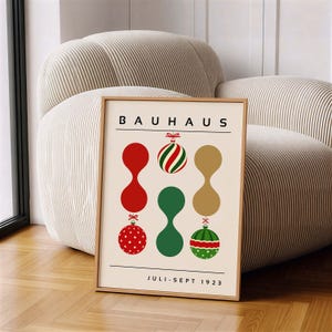 May include: A framed poster with a cream background featuring the text BAUHAUS at the top and JULI-SEPT 1923 at the bottom. The design includes three vertical columns of abstract shapes and Christmas ornaments in red, green, and gold colors.