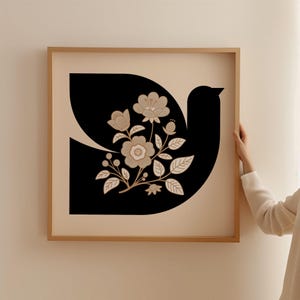 Könnte beinhalten: Ein gerahmter Druck einer schwarzen Silhouette einer Taube mit beigefarbenen floralen Details. Die Taube hält einen Blumenstrauß im Schnabel. Die Blumen sind stilisiert und haben eine Vintage-Ästhetik.