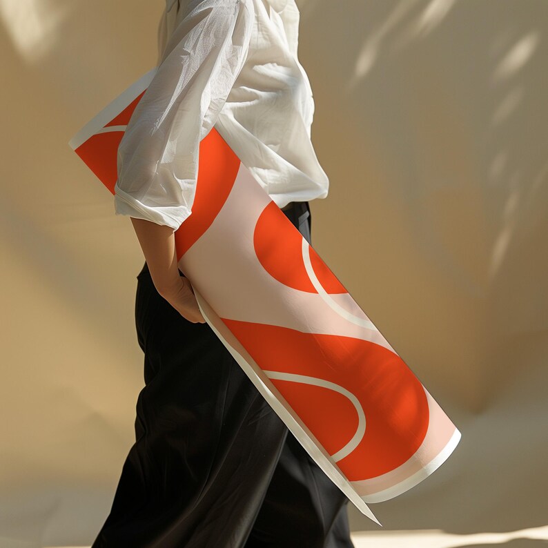 May include: A rolled art print with an abstract design in orange, white, and pale pink. The print is held by a person wearing a white shirt and black trousers. The design features large, curved shapes. The print is rolled up.