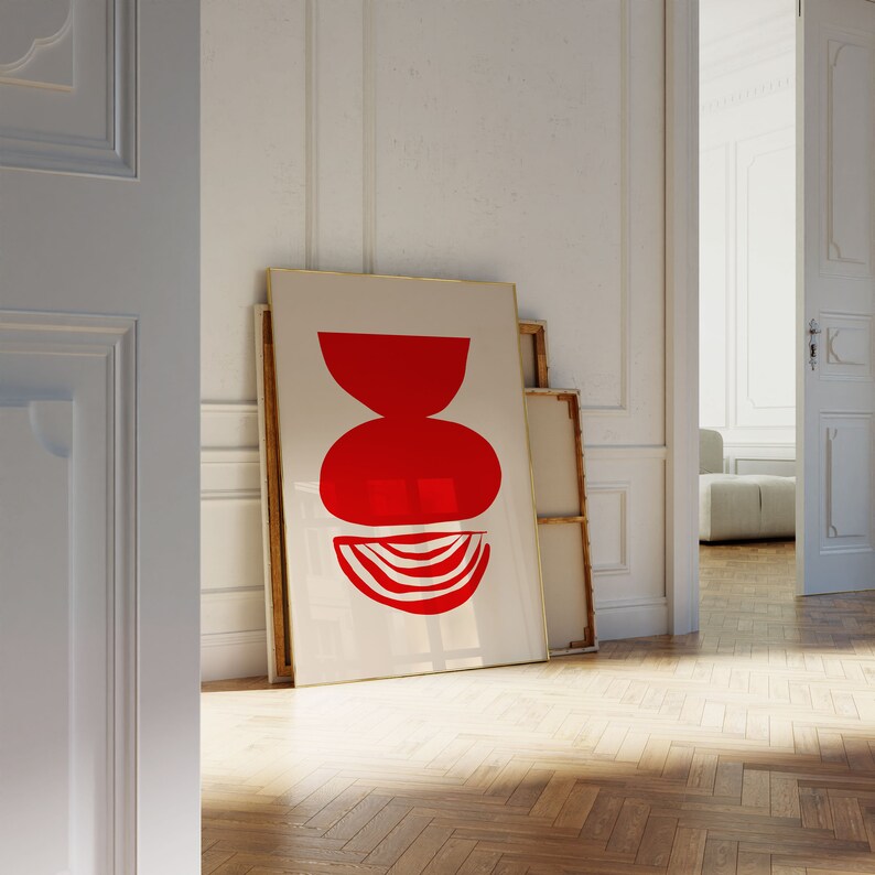 May include: A framed abstract art print with a red geometric design on a white background. The print is leaning against a white wall.