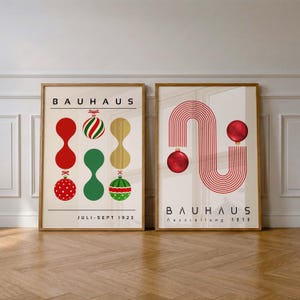 May include: Two framed posters with cream backgrounds. The left poster features the text BAUHAUS, JULI-SEPT 1923, and abstract shapes with red, green, and gold Christmas ornaments. The right poster displays BAUHAUS, Ausstellung 1919, and red lines.
