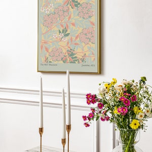 May include: A framed print of a floral pattern in shades of pink, green, and yellow. The print is titled "Jasmine, 1872" and is attributed to William Morris. The print is displayed on a white wall above a table with candlesticks and a vase of flowers.