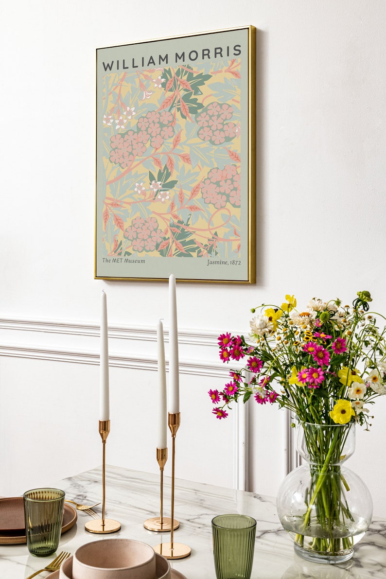 May include: A framed print of a floral pattern in shades of pink, green, and yellow. The print is titled "Jasmine, 1872" and is attributed to William Morris. The print is displayed on a white wall above a table with candlesticks and a vase of flowers.