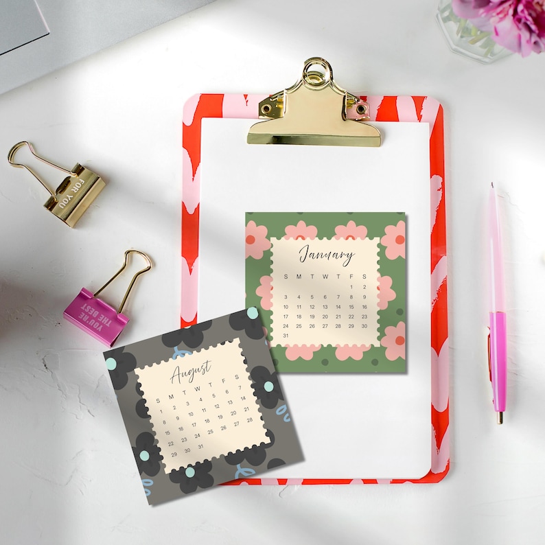 May include: A clipboard with a red and pink heart pattern, a gold clip, and two square calendar pages. One page shows January with pink flowers on a green background, and the other shows August with black flowers on a dark gray background.