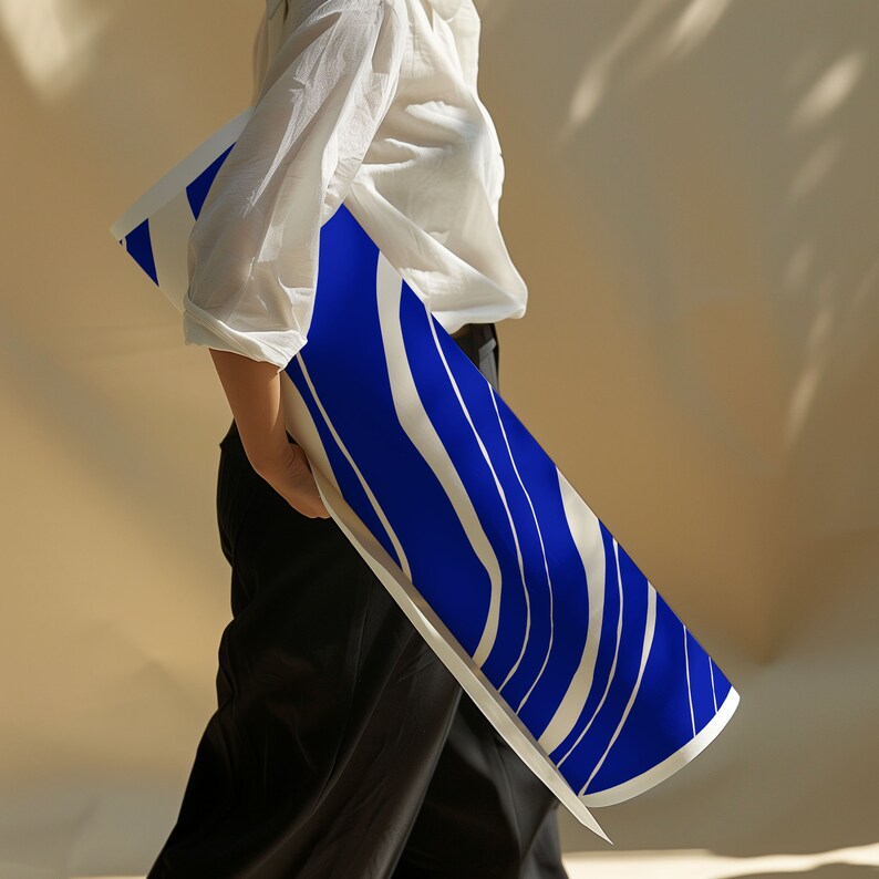May include: A long, rectangular scarf featuring a striking blue and white wavy stripe design. The scarf is held by someone wearing a white blouse and black trousers. The scarf's pattern is contemporary and visually appealing.