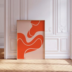 May include: A framed abstract art print with a design of flowing orange shapes with white outlines on a light pink background. The artwork is displayed in a room with white walls and a wooden floor.