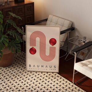 May include: A rectangular framed poster featuring a graphic design of red concentric lines forming an S-shape with two red spherical ornaments attached to the ends. The text BAUHAUS Ausstellung 1919 is printed in black at the bottom.