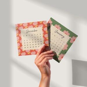 May include: Two square calendar cards featuring the months of December and January. The December card has a red background with pink flower patterns, while the January card has a green background with pink flowers. Both display black text.
