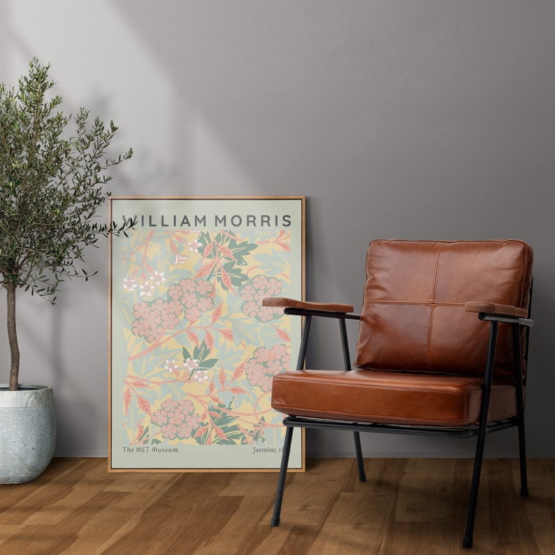 May include: A brown leather armchair with a black metal frame sits on a wooden floor. A poster with the text "WILLIAM MORRIS" and a floral design hangs on the wall behind the chair. The poster is from The MET Museum and features a design called "Jasmine I."