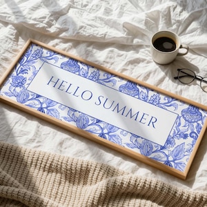 Puede incluir: Un letrero rectangular con marco de madera con las palabras "HELLO SUMMER" en azul marino. El letrero tiene un fondo blanco con un patrón floral azul. Una taza de café y gafas están al lado del letrero.