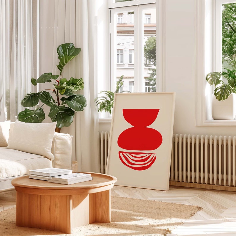 May include: A minimalist abstract art print with a red geometric shape design on a white background. The print is framed and hanging on a white wall in a living room setting.