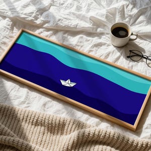 Puede incluir: Una bandeja rectangular de madera con un diseño náutico. La bandeja presenta un patrón de olas azules y turquesas con un barco de papel blanco. Una taza de café y gafas están al lado de la bandeja sobre una superficie blanca.