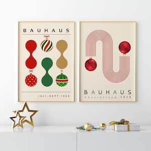 May include: Two framed posters with cream backgrounds. The left poster features the text BAUHAUS and JULI-SEPT 1923 with red, green, and gold abstract shapes and Christmas ornaments. The right poster features BAUHAUS AUSSTELLUNG 1919 with red lines and ornaments.