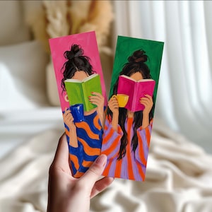 Può includere: Due segnalibri rettangolari con illustrazioni di persone con capelli scuri raccolti in uno chignon che leggono libri. Uno ha uno sfondo rosa con un libro verde e una tazza blu, l'altro uno sfondo verde con un libro rosa e una tazza gialla.