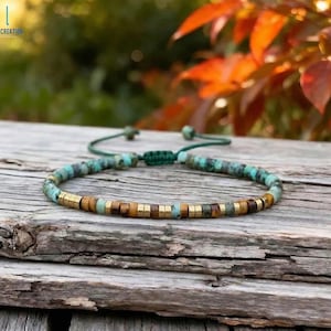 May include: A beaded bracelet with turquoise and brown beads, interspersed with gold-colored square beads. The bracelet is on a wooden surface. The bracelet has a green adjustable cord. The brand name "LIZ CREATION" is in the top left corner.