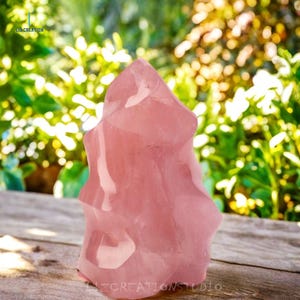May include: A large, pink, rose quartz crystal with a unique, faceted, and irregular shape. The crystal is sitting on a wooden surface.