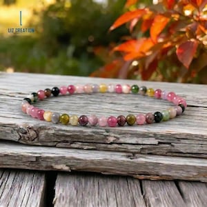 Puede incluir: Una delicada pulsera de cuentas con pequeñas piedras preciosas de turmalina redondas y lisas en una variedad de colores, incluyendo rosa, verde, amarillo y negro. Las cuentas están ensartadas en una sola hebra, creando un accesorio circular fino.