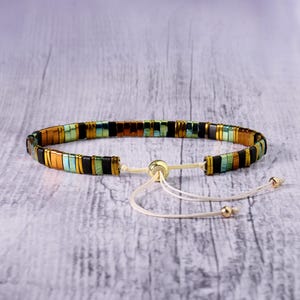 Op de afbeelding: Een veelkleurige kralen armband met een schuifknoop sluiting. De armband heeft zwarte, bruine, groene en gouden kralen.