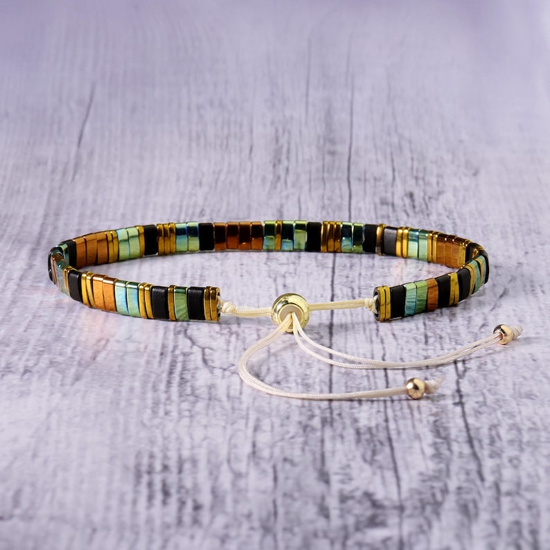 Op de afbeelding: Een veelkleurige kralen armband met een schuifknoop sluiting. De armband heeft zwarte, bruine, groene en gouden kralen.
