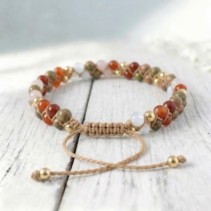 May include: Adjustable macrame bracelet featuring a variety of colorful gemstone beads, including red, green, and pink stones, interspersed with gold-colored beads. The bracelet is tied with a natural-colored cord and has a sliding knot closure.