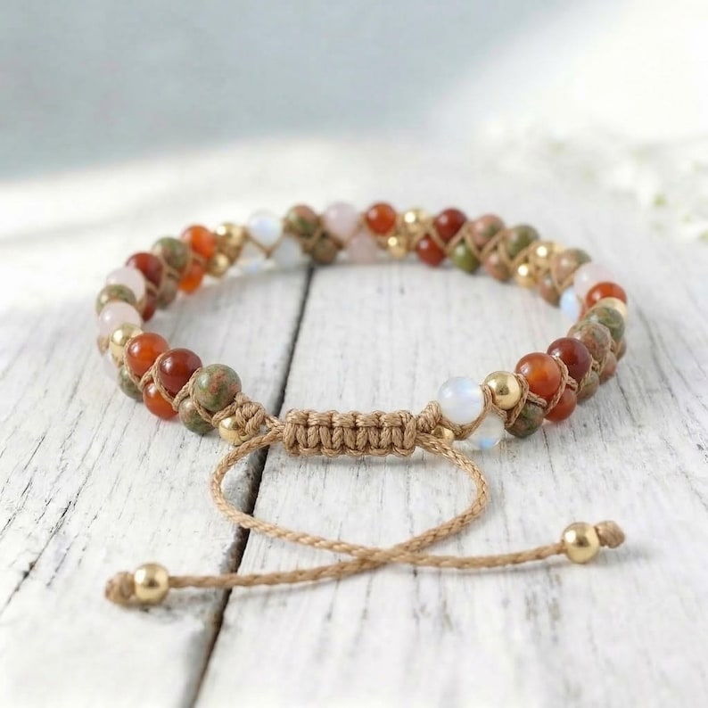 May include: Adjustable macrame bracelet featuring a variety of colorful gemstone beads, including red, green, and pink stones, interspersed with gold-colored beads. The bracelet is tied with a natural-colored cord and has a sliding knot closure.