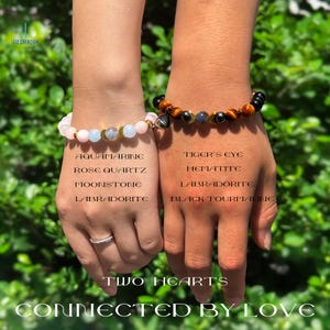 Pode incluir: Dois pulsos exibem pulseiras de pedras preciosas. Uma apresenta contas de &aacute;gua-marinha, quartzo rosa, pedra da lua e labradorita. A outra apresenta olho de tigre, hematita, labradorita e turmalina negra. O texto diz "TWO HEARTS CONNECTED BY LOVE."