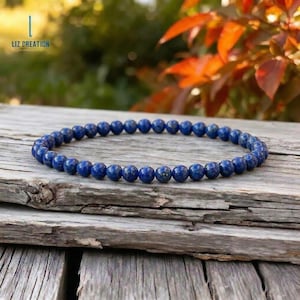 Op de afbeelding: Een donkerblauwe kralenarmband gemaakt van ronde stenen. De armband wordt gepresenteerd op een verweerd houten oppervlak. De tekst "LIZ CREATION" staat in de linkerbovenhoek.