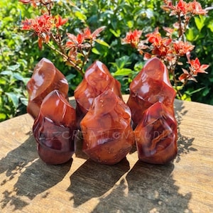 May include: Six red carnelian crystal points with a swirling, marbled pattern. The points are arranged in a cluster on a wooden surface.