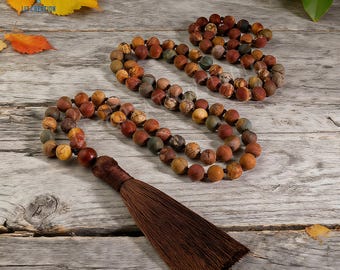 May include: A set of three mala prayer beads with a brown tassel. The beads are a mix of earth-toned colors, including brown, tan, and green. The beads are strung together on a dark cord. The tassel is a dark brown color.