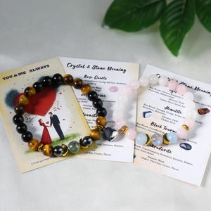 Pode incluir: Duas pulseiras de contas com diferentes tipos de pedras, incluindo &ocirc;nix preto, olho de tigre e quartzo rosa. As pulseiras s&atilde;o exibidas com cart&otilde;es informativos sobre os significados dos cristais. Os cart&otilde;es t&ecirc;m texto e ilustra&ccedil;&otilde;es.