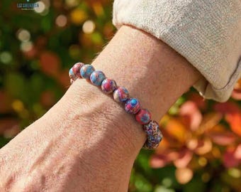 Pode incluir: Uma pulseira de contas redondas multicoloridas, em tons de azul, vermelho e bege. A pulseira é usada no pulso. O nome da marca "LIZ CREATION" é visível no fundo. As contas têm cerca de 1 cm de diâmetro.