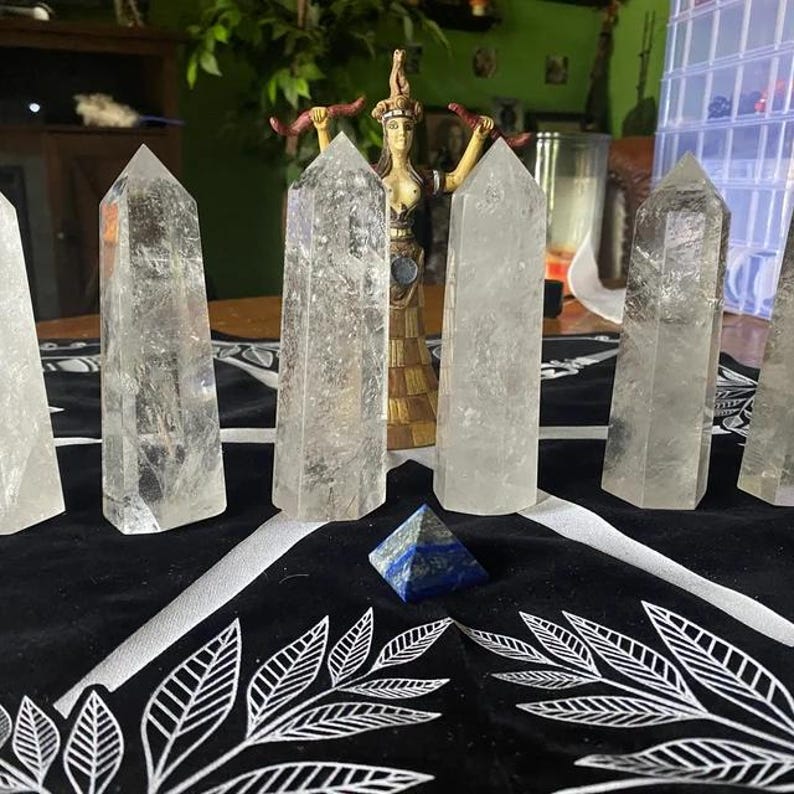 Puede incluir: Siete puntas de cristal de cuarzo transparente dispuestas en c&iacute;rculo sobre una superficie con estampado blanco y negro. Una pir&aacute;mide de lapisl&aacute;zuli azul se encuentra en el centro del c&iacute;rculo.